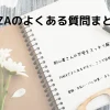 ノートの上にメガネと白い花が置かれたやさしい雰囲気の写真。FANZAのよくある質問をまとめたガイドページの表紙。